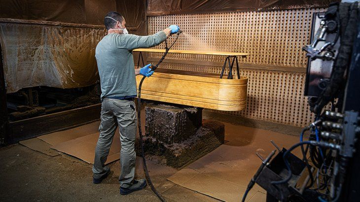 Área de barnizado de los féretros. La cadena humana no se detiene y los empleados deben barnizar un ataúd tras otro apenas los reciben de la sección anterior.