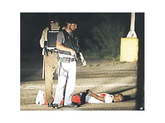 Un joven negro yace herido en un estacionamiento en Ferguson, en el contexto de tiroteos entre bandas y con la Policía en el primer aniversario del asesinato de Michael Brown por agentes de seguridad. Vuelve la tensión racial en esa conflictiva ciudad.