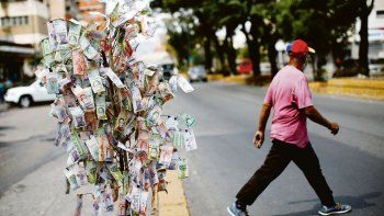 sin valor. Un hombre pasa junto a una suerte de árbol hecho con billetes de bolívar en Caracas.&nbsp;