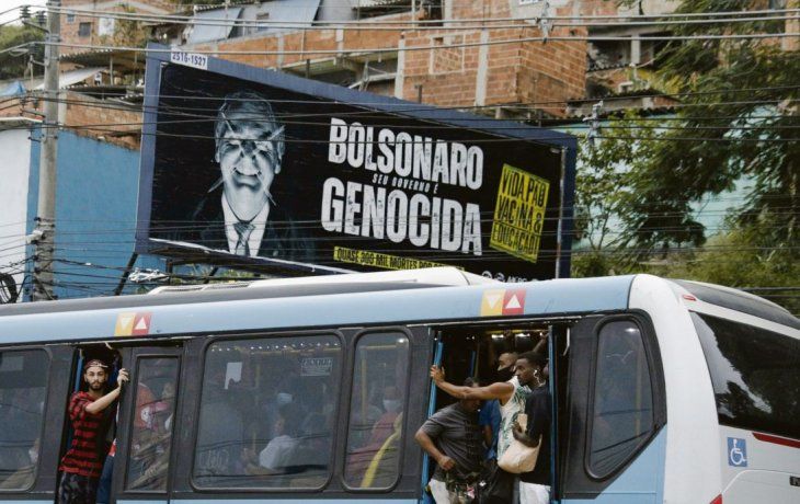 CLAMOR. La acusación de que Jair Bolsonaro está cometiendo un genocidio en Brasil por su negacionismo en torno a la pandemia gana la calle en ese país, como se ve en el cartel junto al que pasa un colectivo abarrotado en Río de Janeiro.