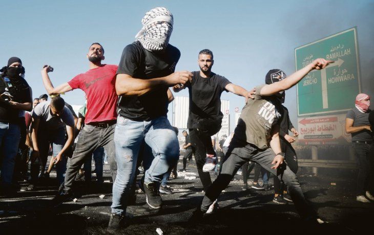TENSIÓN. Un grupo de jóvenes arrojan piedras contra soldados israelíes en Cisjordania. La protesta tuvo lugar días después de que se registraran violentos choques en las ciudades mixtas de Israel.