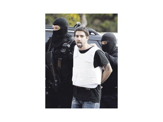 Un detenido por la ola de envíos de paquetes bomba a embajadas en Atenas es trasladado por la Policía. Uno de los despachos llegó a la Jefatura de Gobierno en Alemania.