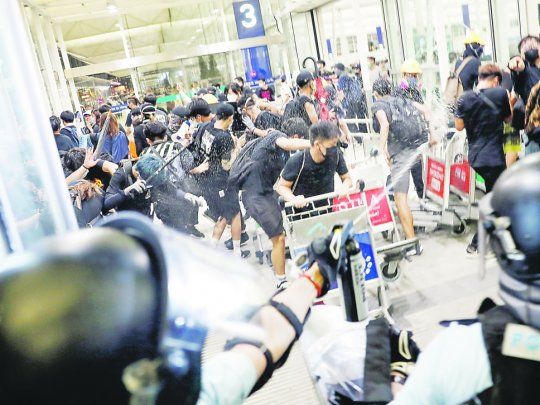 CHOQUES. La policía hongkonesa reprimió con gas pimienta a los manifestantes dentro del aeropuerto. Ellos atacaron a dos personas, que debieron ser hospitalizadas, por considerarlas espías.