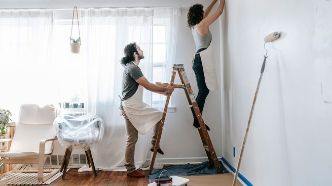 Una pareja pinta una de las paredes del living de su casa, recientemente renovado