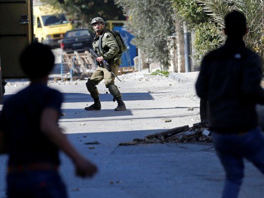 Manifestantes palestinos se preparan para arrojar piedras a un soldado israel&iacute;.