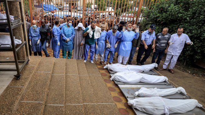 Hombres oran ante algunos de los cuerpos de las víctimas que murieron en el bombardeo israelí.
