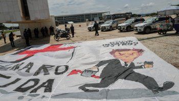 REPUDIO. Policías retiran una bandera que tacha a Jair Bolsonaro de nazi y genocida, colocada a las puertas del Palacio del Planalto de Brasilia por un grupo de personas que rechazan sus posturas anticientíficas en la pandemia.