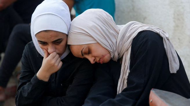 Dos mujeres lloran en el funeral de un civil asesinado al buscar ayuda humanitaria en Gaza.
