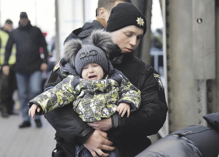 DRAMA HUMANITARIO. Un policía ucraniano carga a un niño en momentos en que residentes de la ciudad de Lviv se concentraban en la estación de trenes para huir a Polonia.