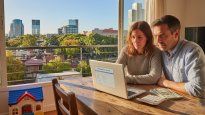 Una pareja en el departartamento que alquilan en Saavedra con calculadora y dólares sobre la mesa explora opciones de créditos hipotecarios en la computadora, el sueño de la casa propia es posible