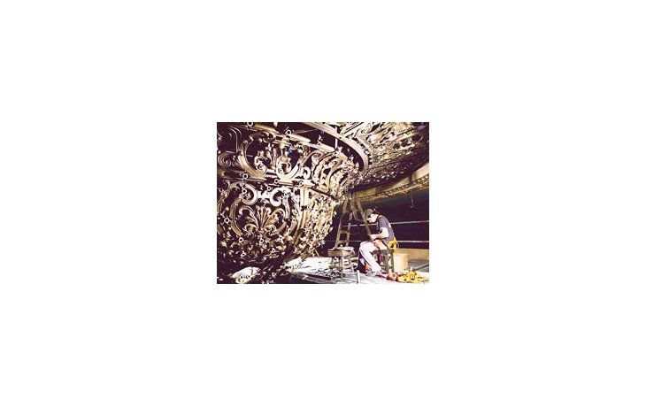Un operario trabaja en la restauración de la araña central de la sala.