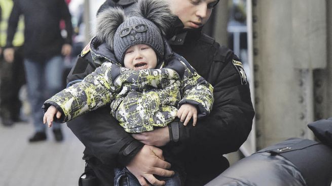 DRAMA HUMANITARIO. Un policía ucraniano carga a un niño en momentos en que residentes de la ciudad de Lviv se concentraban en la estación de trenes para huir a Polonia.