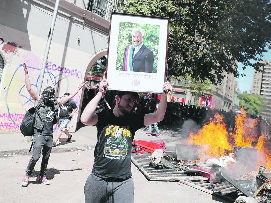 Incendio. Un manifestante muestra un retrato del presidente Sebasti&aacute;n Pi&ntilde;era frente a una barricada. Anoche, al inicio del estado de excepci&oacute;n, se reportaban nuevos incidentes.&nbsp;