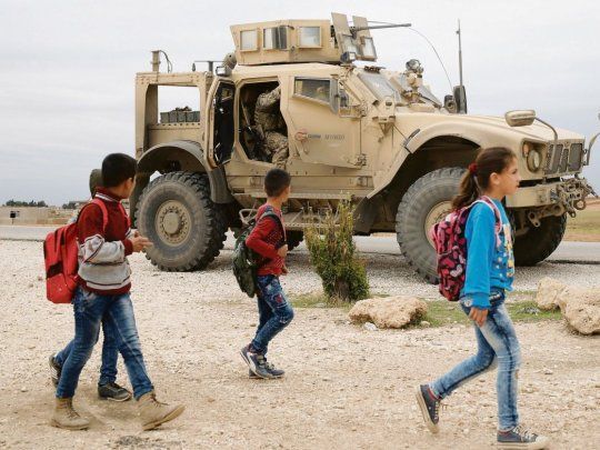 vigilancia. Escolares sirios caminan en una zona cercana a la frontera con Turquía bajo la protección de un vehículo y soldados de Estados Unidos. La zona fue arrebatada al Estado Islámico, pero la situación aún es fluida.
