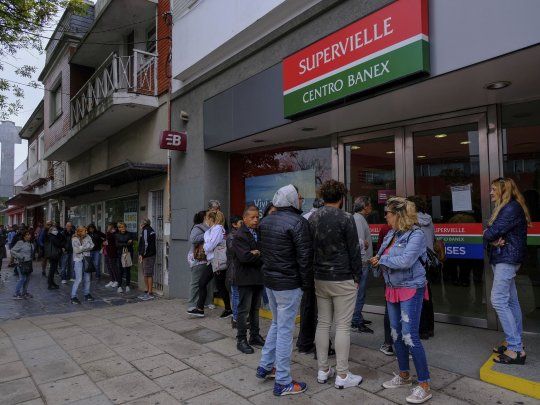 La gente hace largas filas en las puertas de los bancos para retirar dinero.