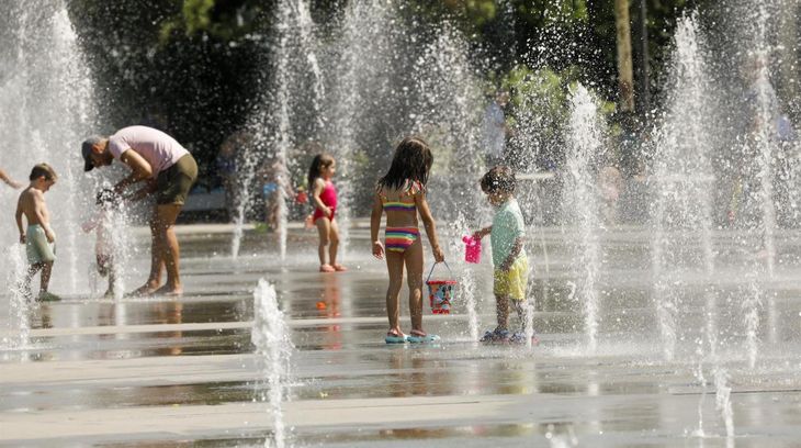 Un grupo de niños se refugia del calor jugando en una fuente de agua.