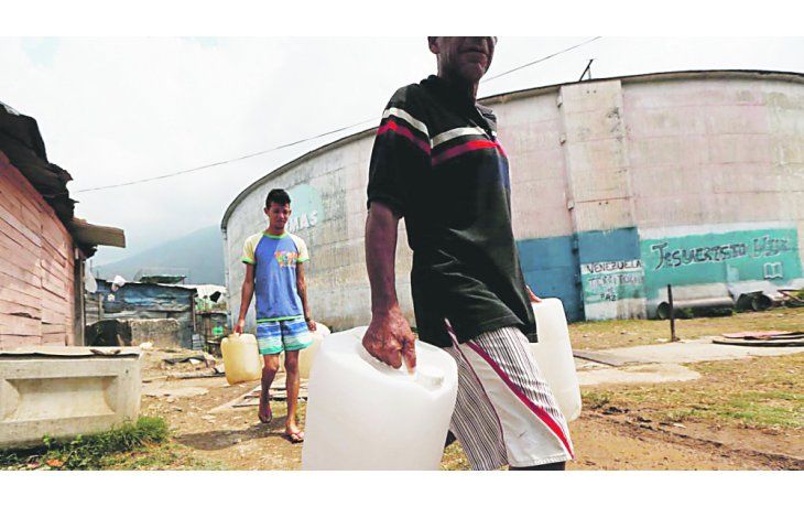 ámbito.com | PRECARIEDAD. Dos venezolanos caminan, bidones en mano, para buscar agua para sus hogares en la ciudad de Puerto Ordaz.
