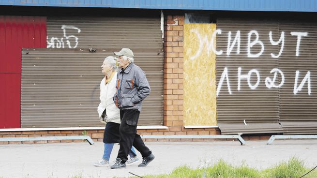 CONTROL. Un tanque ruso ataca un blanco cerca de la zona industrial donde se refugian civiles en Mariúpol. En la ciudad, asediada desde febrero, aún habitan miles de personas. En la calle, se lee en las persianas bajas de un comercio “acá vive gente”.