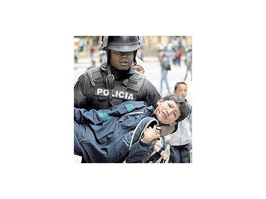 Un polícía lleva a un niño herido en los nuevos enfrentamientosprovocados ayer en Quito por seguidores del presidenteRafael Correa. La aplicación de un chavismo a la ecuatorianaestá provocando una convulsión política.