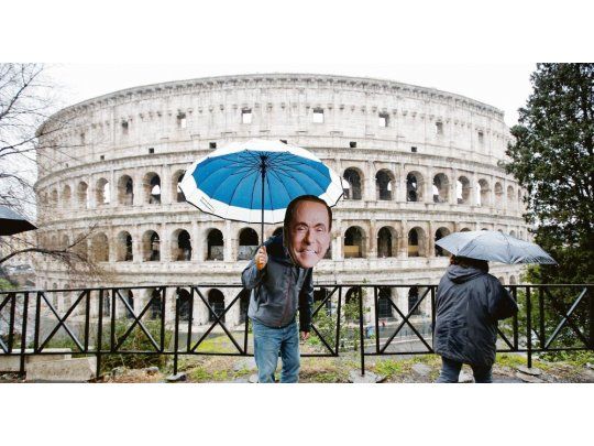 TORMENTA. Roma amaneció ayer cubierta por nubes. En las inmediaciones del Coliseo, un hombre saluda a los transeúntes con una máscara de Silvio Berlusconi.