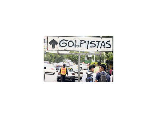 Hondureños caminan cerca de un cartel contrario al golpe de Estado.