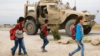 vigilancia. Escolares sirios caminan en una zona cercana a la frontera con Turquía bajo la protección de un vehículo y soldados de Estados Unidos. La zona fue arrebatada al Estado Islámico, pero la situación aún es fluida.