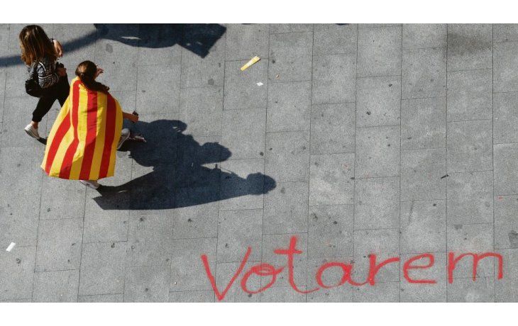 ámbito.com | Voluntad. Dos jóvenes independentistas catalanes caminan junto a una pintada en el suelo que dice, en la lengua local, “votaremos”.
