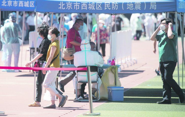 REFUERZO. Un trabajador sanitario protegido por un traje especial realiza exámenes de Covid-19 en un estadio, después del nuevo brote registrado en Pekín.