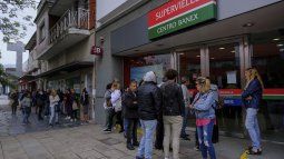 La gente hace largas filas en las puertas de los bancos para retirar dinero.
