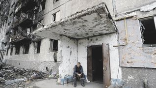 DEMOLICIÓN. Un hombre toma asiento en un edificio residencial destruido por los combates, mientras personal sanitario retira los cadáveres en Mariúpol.