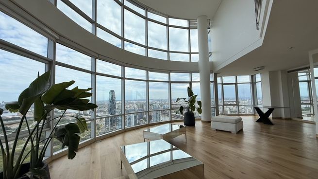 Living de grandes dimensiones en Puerto Madero con doble altura y ventanales curvos que ofrecen vistas panorámicas de la Ciudad y el río