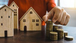 Una mano sostiene monedas y pequeñas casas de madera, símbolo del ahorro y del acceso al crédito hipotecario en un contexto de ajuste de tasas y mayores exigencias Una mano sostiene monedas y pequeñas casas de madera, símbolo del ahorro y del acceso al crédito hipotecario en un contexto de ajuste de tasas y mayores exigencias