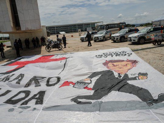 REPUDIO. Policías retiran una bandera que tacha a Jair Bolsonaro de nazi y genocida, colocada a las puertas del Palacio del Planalto de Brasilia por un grupo de personas que rechazan sus posturas anticientíficas en la pandemia.