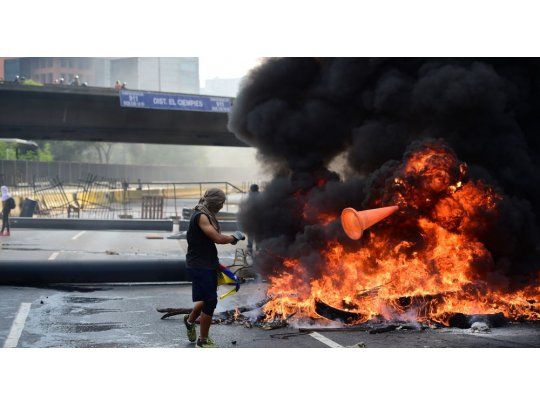 Manifestante de la oposición arroja un cono al fuego de una barricada realizada en Caracas.