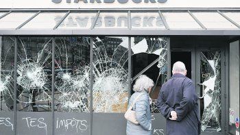ATÓNITOS. Una pareja mira los destrozos en un Starbucks en París. Ayer, decenas de comerciantes volvieron a sus locales para tapiarlos y hacer un registro del daño ocasionado durante la manifestación del sábado.