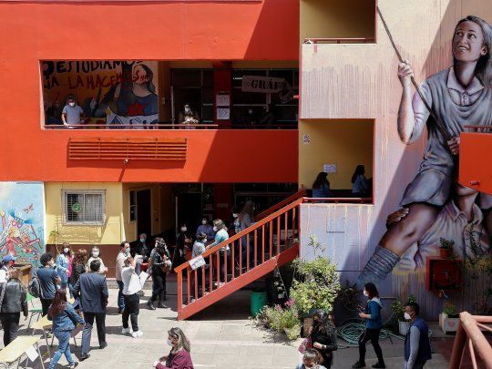 SÍMBOLOS. Las urnas abiertas, votantes acudiendo con barbijos para evitar el nuevo coronavirus y un mural que evoca las protestas de los estudiantes chilenos, imágenes combinadas ayer en una escuela de Valparaíso.