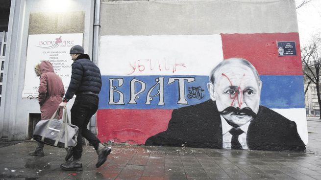 DESPRECIO. Personas caminan delante de un mural del presidente ruso Vladímir Putin que ha sido vandalizado con aerosol con la palabra “asesino”. Originalmente decía “hermano”.