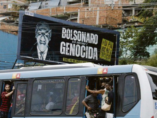 CLAMOR. La acusación de que Jair Bolsonaro está cometiendo un genocidio en Brasil por su negacionismo en torno a la pandemia gana la calle en ese país, como se ve en el cartel junto al que pasa un colectivo abarrotado en Río de Janeiro.