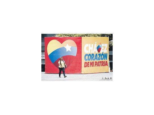 Una mujer camina delante de un cartel proselitista de Hugo Chávez. Otro sondeo le da una ventaja superior a 30 puntos, pero uno apunta un empate.