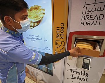 Un joven toma su pan gratis de una expendedora en Dubái.