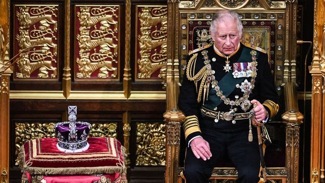 El príncipe Carlos sentado al lado de la corona de su madre, la reina Isabel II.