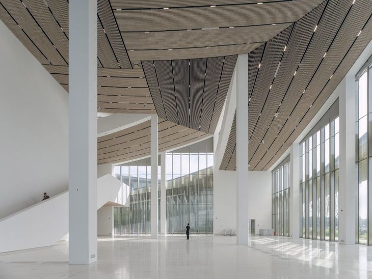 Interior del Museo de Arte Contemporáneo de Suzhou: un gran espacio expositivo atravesado por luz natural, con estructura blanca y cielorrasos de madera Interior del Museo de Arte Contemporáneo de Suzhou: un gran espacio expositivo atravesado por luz natural, con estructura blanca y cielorrasos de madera