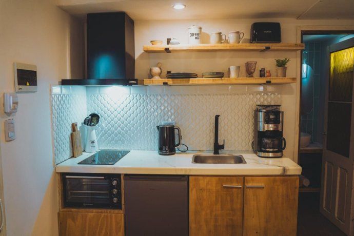 Una cocina compacta, equipada con anafe eléctrico, horno eléctrico, bacha de acero y muebles de madera enchapada. El revestimiento cerámico tipo escama suma textura y refleja la luz Una cocina compacta, equipada con anafe eléctrico, horno eléctrico, bacha de acero y muebles de madera enchapada. El revestimiento cerámico tipo escama suma textura y refleja la luz